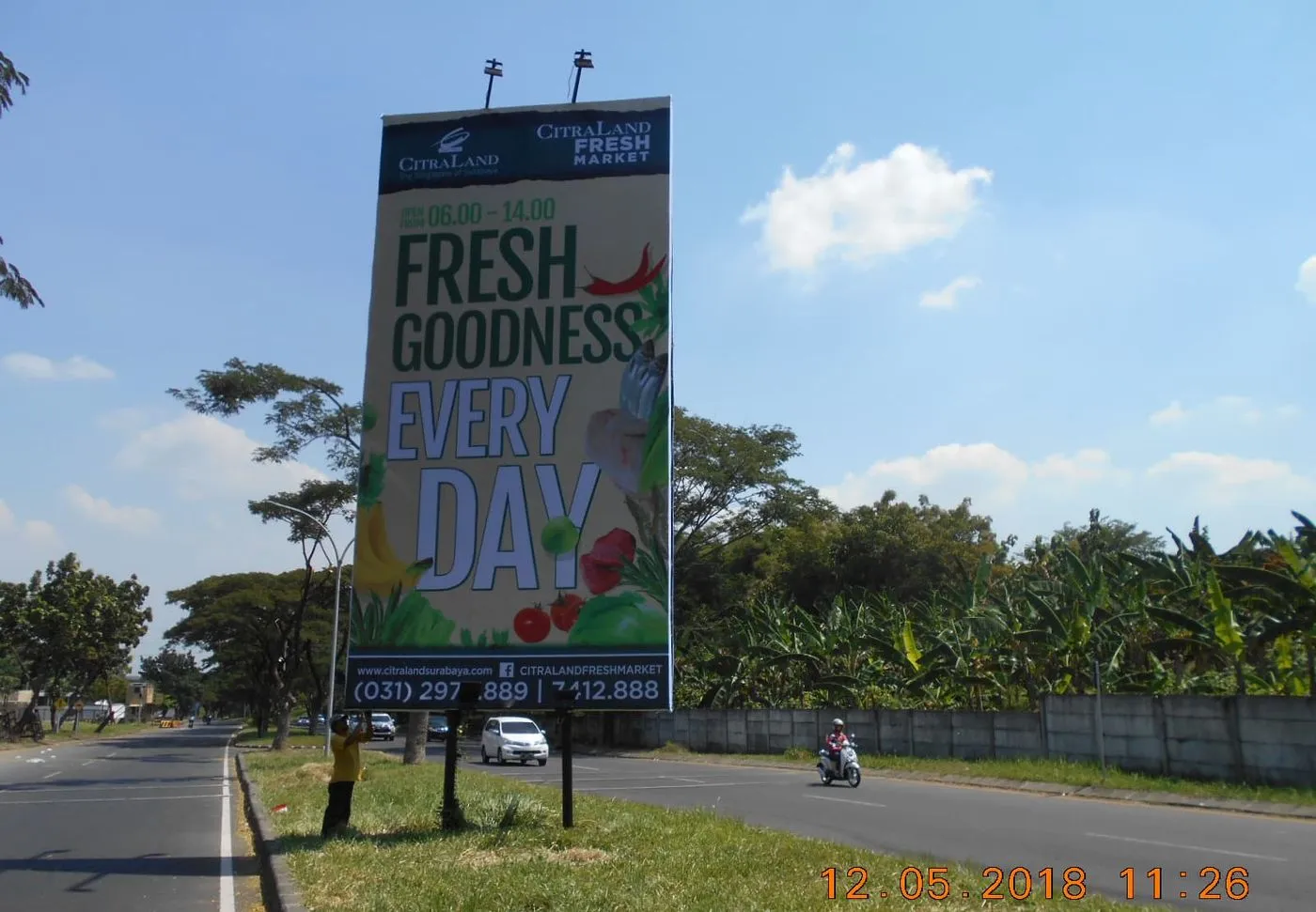 Billboard vertikal CitraLand Fresh Market dengan dua lampu sorot di tepi jalan raya